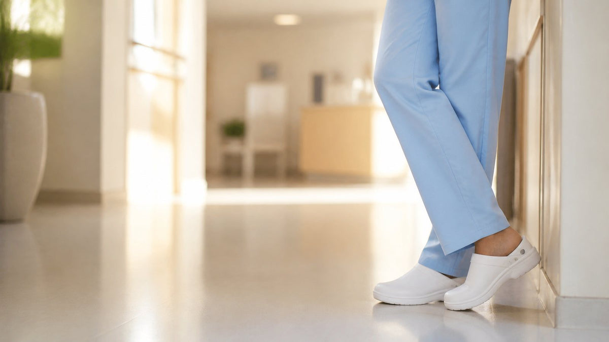 Enfermera de pie en un pasillo de clínica con uniforme azul y suecos blancos cómodos